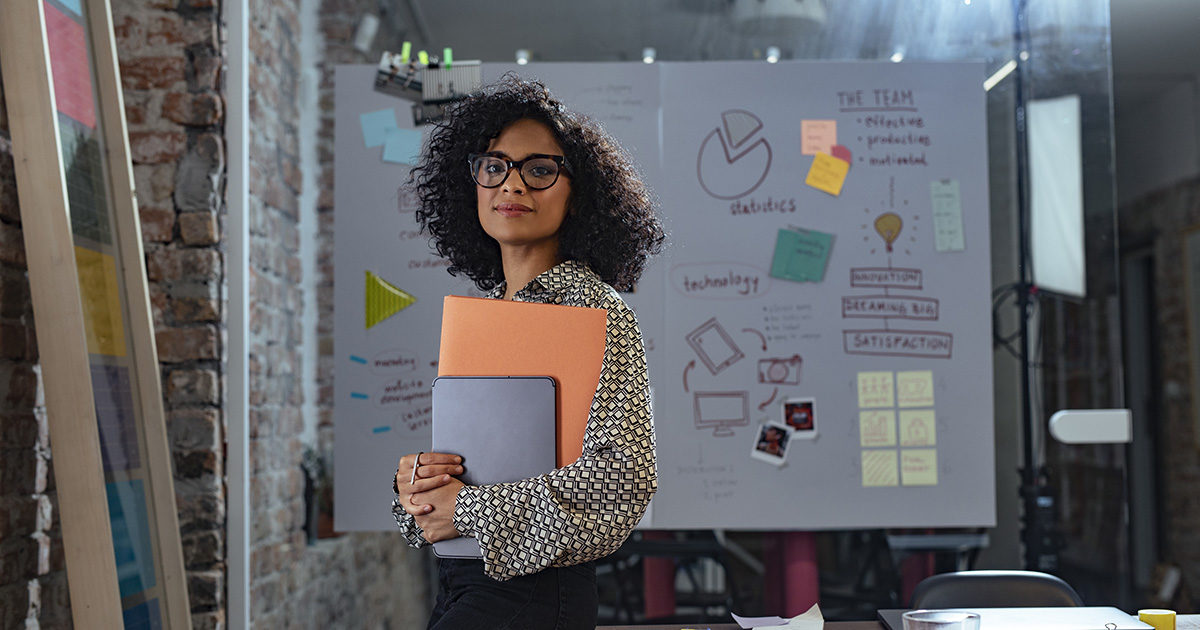 Femme afro-américaine look femme d'affaires souriant devant un tableau de travail, elle tient des documents