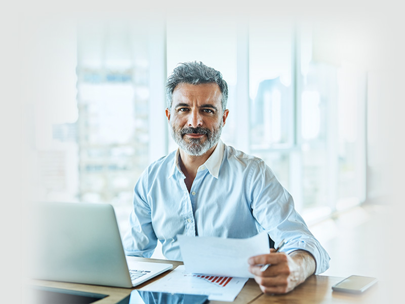 homme cheveux poivre et sel assis devant un bureau ordinateur portable et facture devant lui