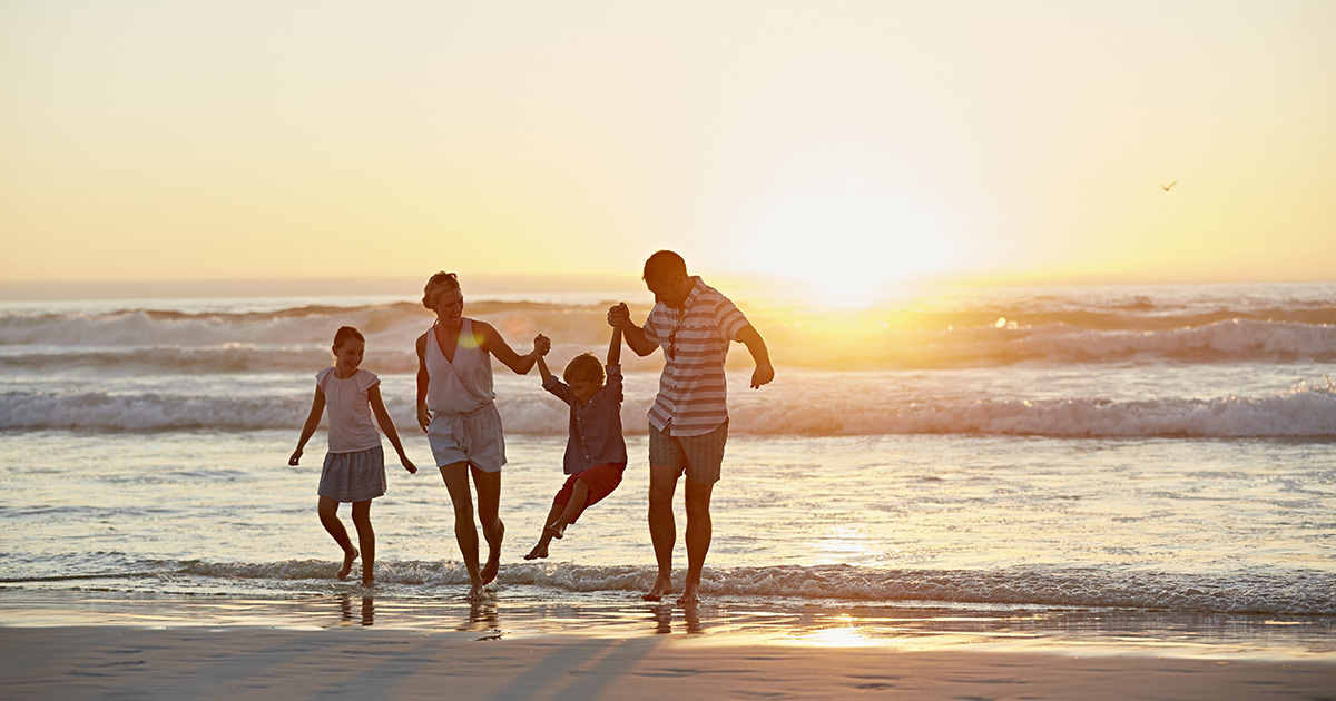 famille 4 personnes père mère et deux enfants. Ils s'amusent sur le bord de la mer devant un magnifique couché de soleil