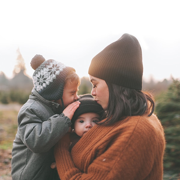 mere avec deux jeunes enfants 3ans et 6 mois dans ses bras. enfant de 3 ans embrasse le bébé. paysage naturel. image de tendresse et de douceur